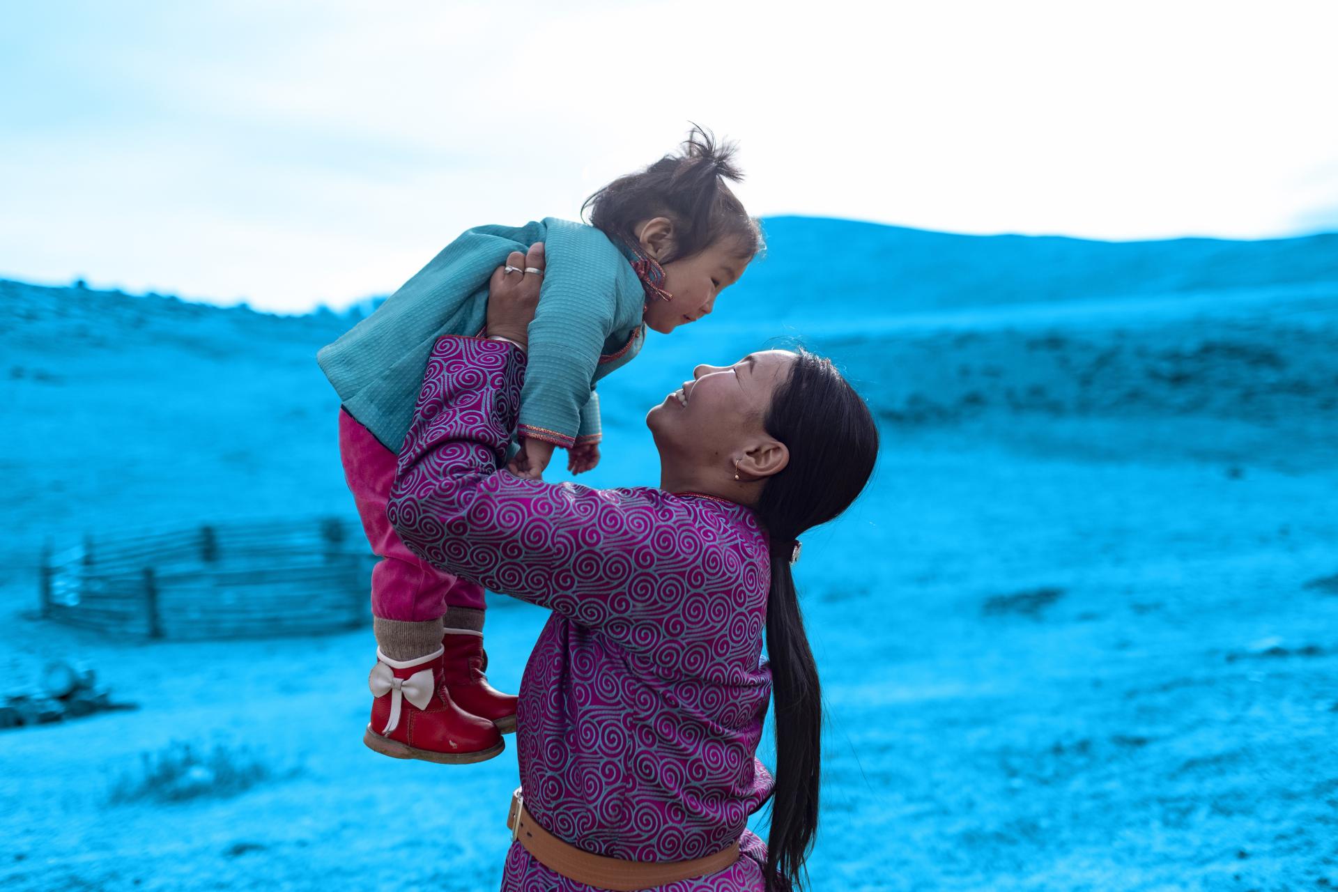 Smiling woman lifting a child in a steppe landscape (decorative for UN Partner Portal article)