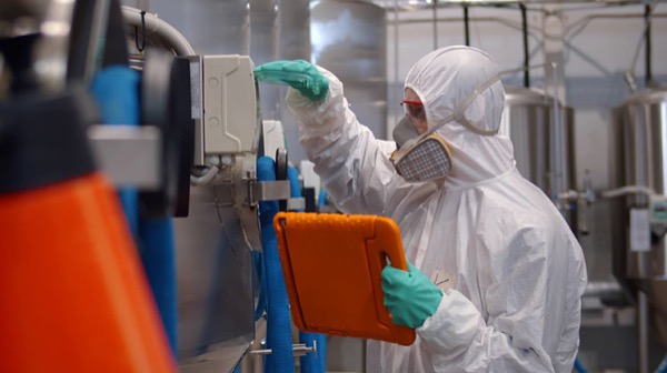 Professional technologist in safety suit and mask using tablet at workshop.