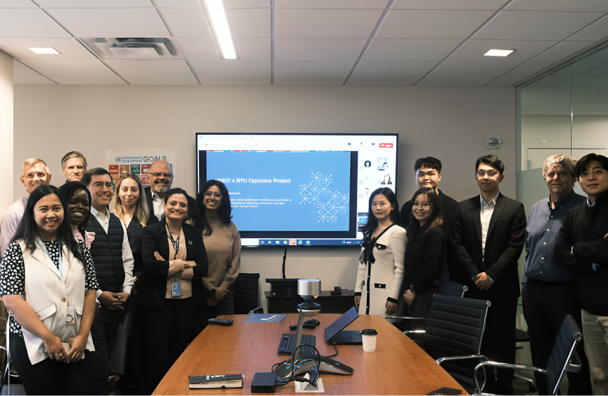 A diverse group of professionals and students posing in a conference room for the UNICC x NYU Capstone Project presentation. A screen in the background displays the project title with a blue slide, and a Sustainable Development Goals poster is visible on the wall. Participants are smiling and dressed in business casual attire, with a mix of in-person and remote attendees shown on the screen.