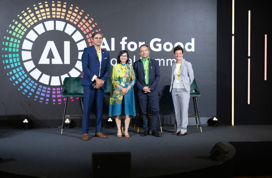 Four panelists stand on stage at the AI for Good Global Summit in front of a large screen displaying the summit's colorful logo and the words “AI for Good Global Summit.”