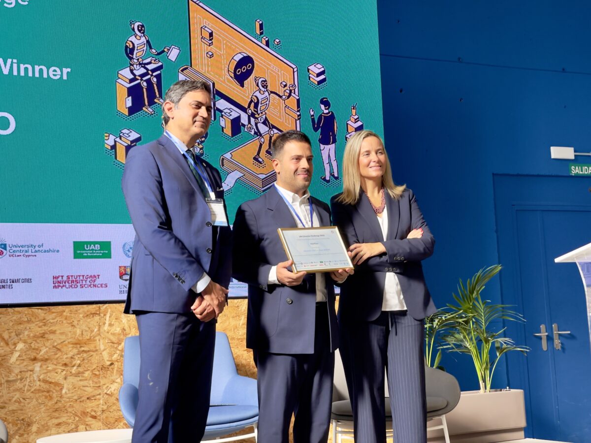 Sameer Chauhan, UNICC Director, stands alongside Paula Llobet Vilarrasa, Councillor for Tourism, Digital Agenda, Innovation and Investment for the City of Valencia, as they present the UN Citiverse Challenge Startup Award to a representative from WEO for its AI-driven solution AURA. The award ceremony takes place on stage during the 1st Citiverse Assembly, with an illustrated digital backdrop behind them.