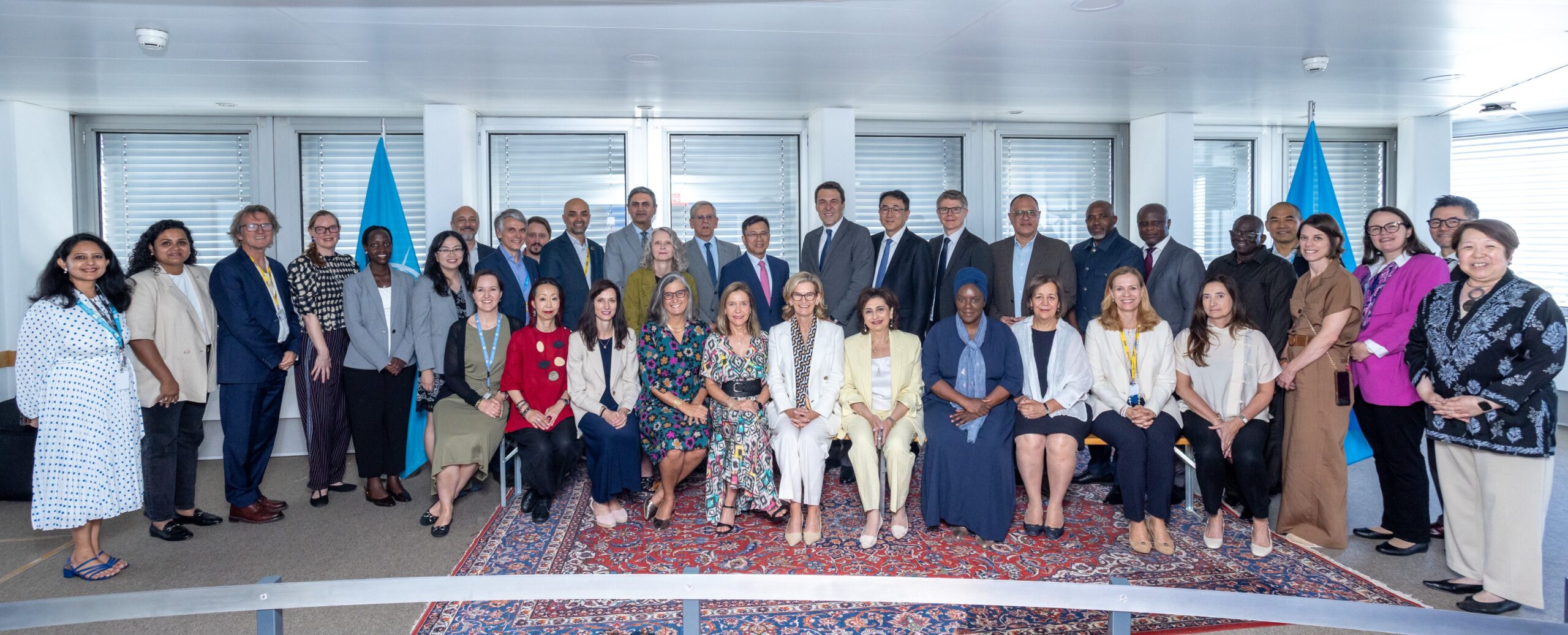 Group photo of participants attending the 23rd UNGIS High-Level Meeting during WSIS Forum 2026 in Geneva, standing and seated together in a conference room with UN flags displayed in the background.