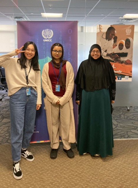 Three individuals pose in front of UNICC banner.