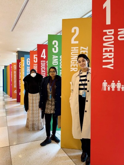 Three participants pose in front of UN SDGs. 