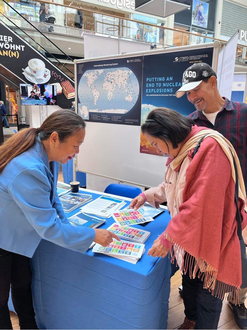 Three people at CTBTO stand looking over UN SDGs. 